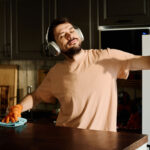 Young man in headphones enjoying music with headphones while standing by kitchen counter and cleaning