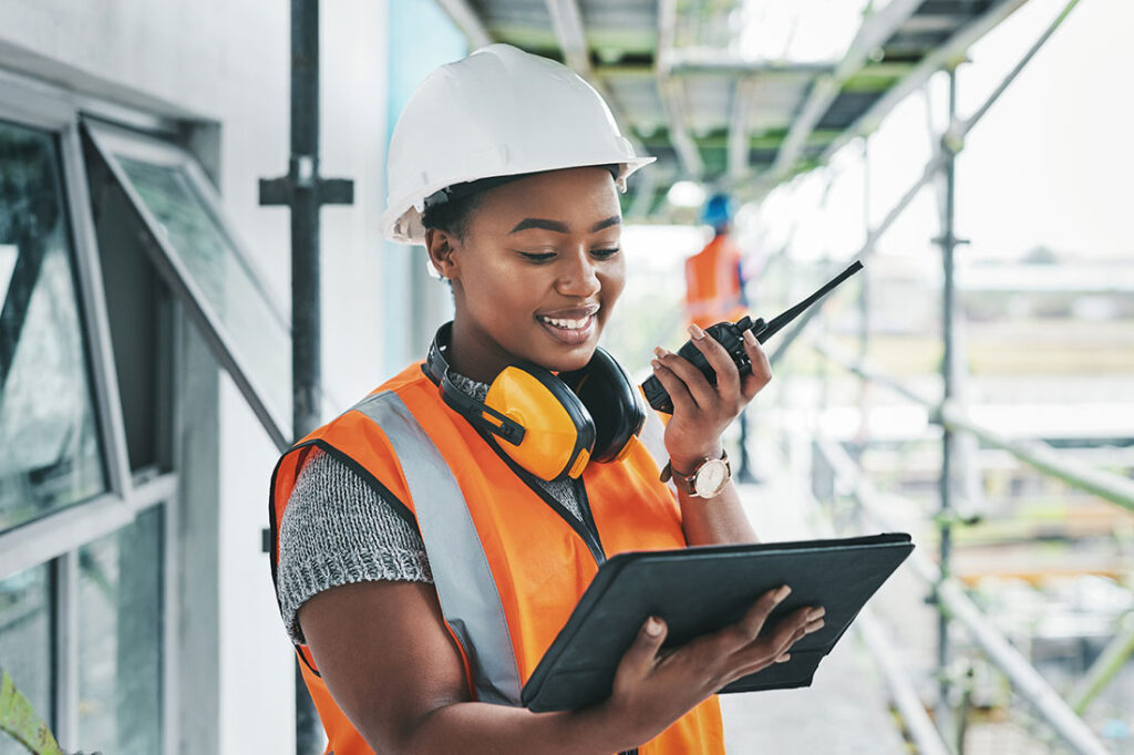 Black woman worker with tablet on a construction site strategy and talking on a walkie talkie.