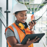 Black woman worker with tablet on a construction site strategy and talking on a walkie talkie.