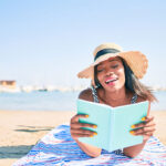 Young african american woman on vacation laying on the towel reading book at the beach