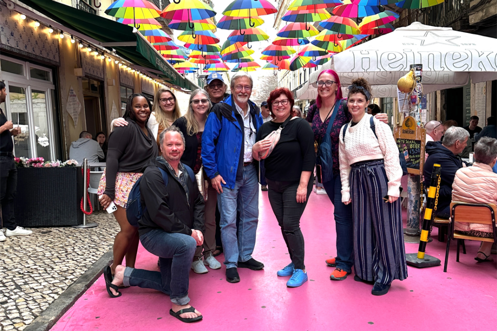 The Expatsi team poses for a photo underneath rows of rainbow umbrellas while standing on a pink road.