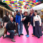 The Expatsi team poses for a photo underneath rows of rainbow umbrellas while standing on a pink road.