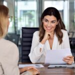 A woman smiles at her employee while looking over a document.