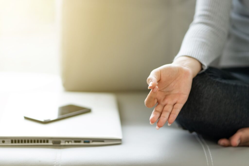 A woman sits in meditation pose next to a closed laptop and phone.