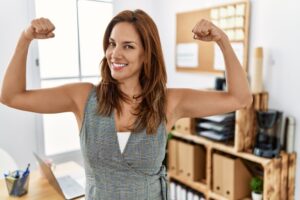 A woman in professional attire flexes her muscles.