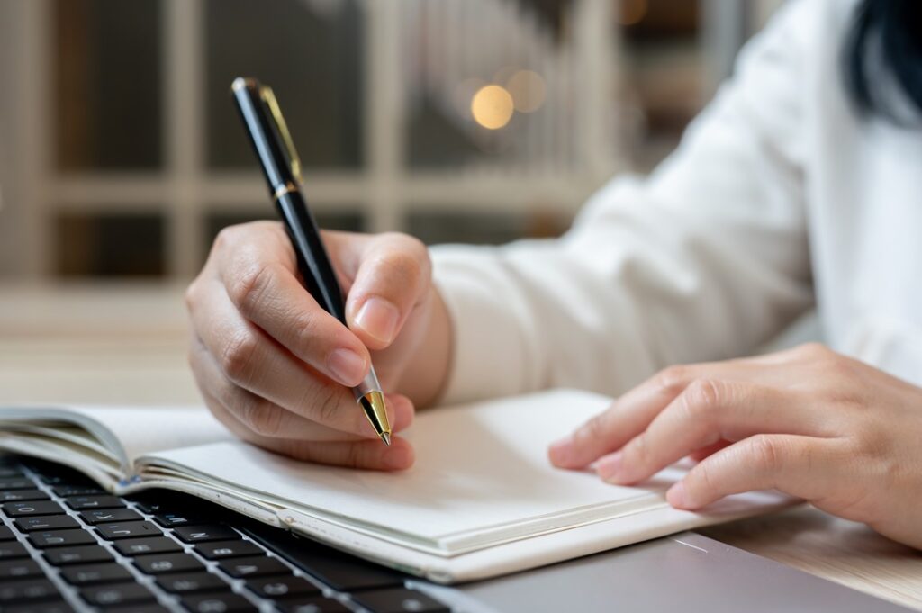 a woman using a pen to write in a notebook