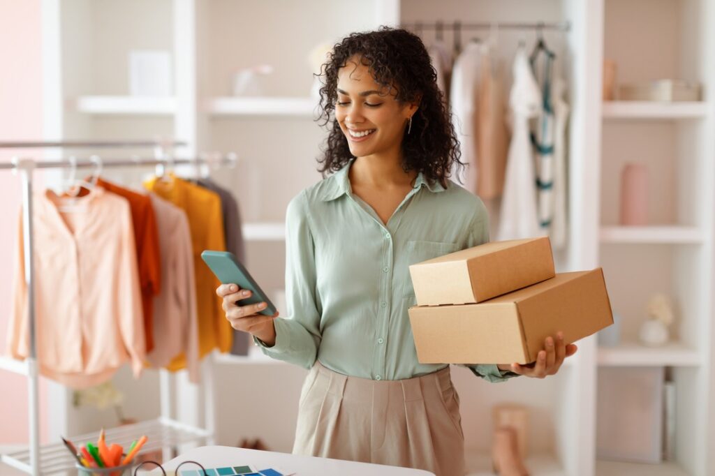 woman using her phone to look up how to create an llc while holding two cardboard boxes in her left hand