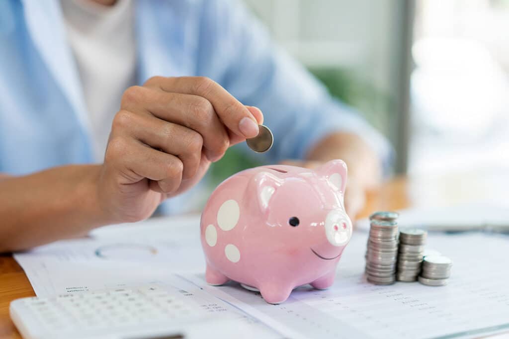 man piling up his coins on the desk and dropping a coin into piggy bank