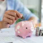 man piling up his coins on the desk and dropping a coin into piggy bank