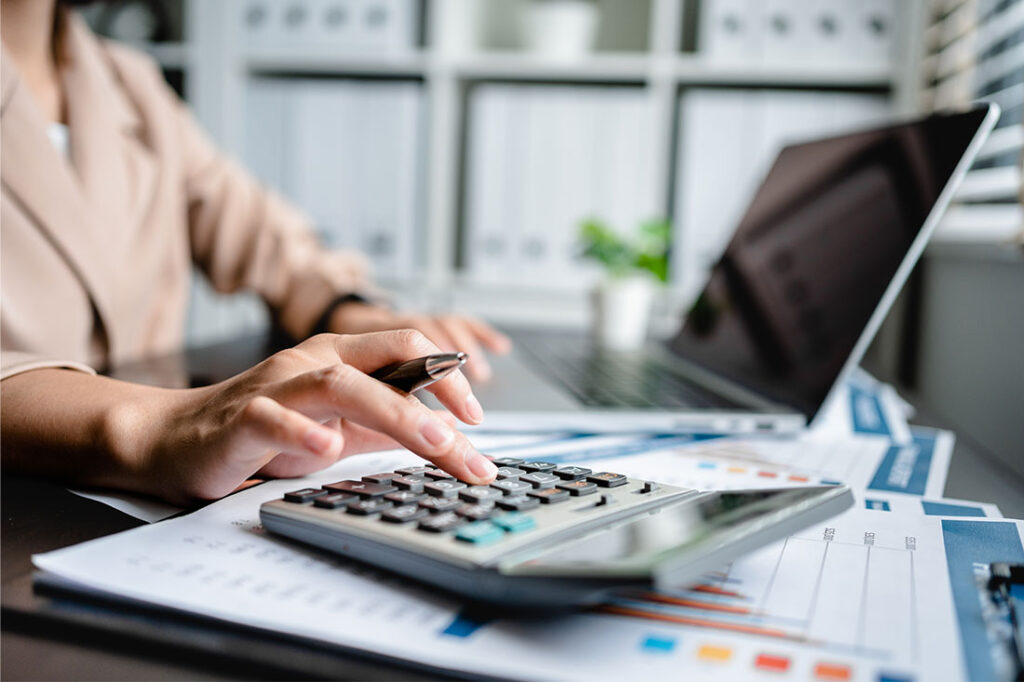 Close up of woman using calculator and a laptop computer to analyze finance and freelance income