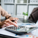 Close up of woman using calculator and a laptop computer to analyze finance and freelance income