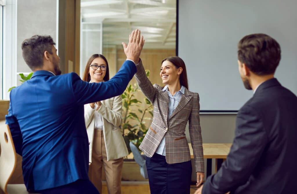 woman giving a high-five to her colleague in the office while other coworkers are facing them