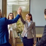 woman giving a high-five to her colleague in the office while other coworkers are facing them