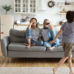 Kids running around father and mother sitting at couch