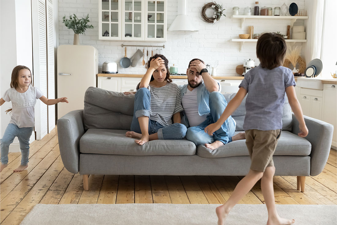 Kids running around father and mother sitting at couch