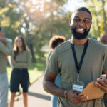 Volunteer with clipboard and group of people in backdrop collecting trash and waste management