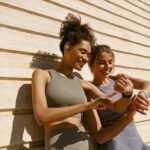 two women smiling while looking at their exercise watches