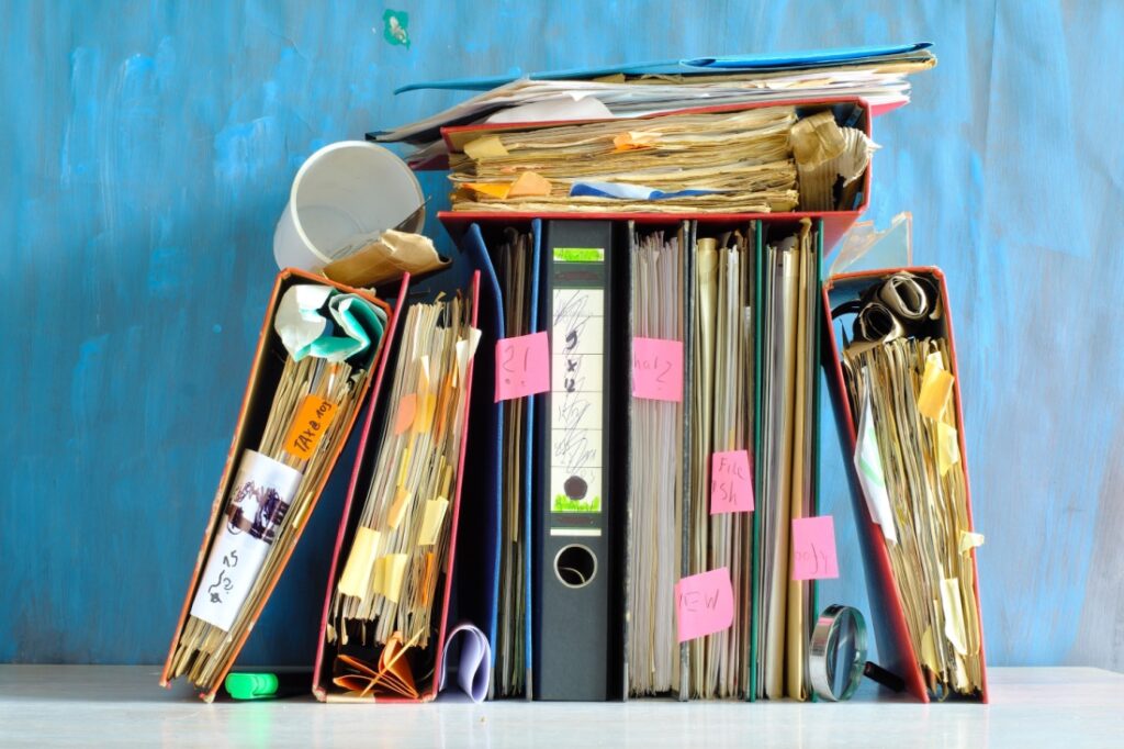 A row of binders full of sticky note and a used coffee cup.