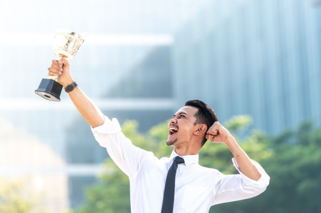 An employee pumps his fist while holding a trophy up in the air.