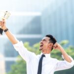 An employee pumps his fist while holding a trophy up in the air.