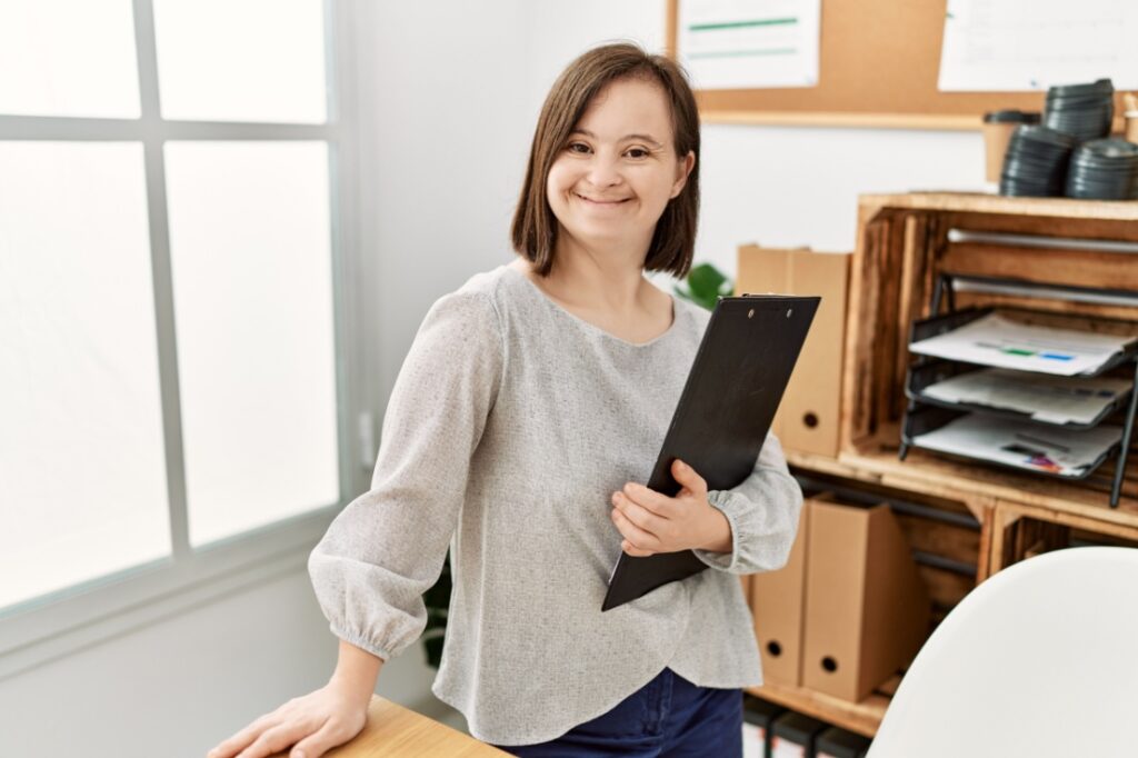 A young woman with down syndrome holds a clipboard in her office.