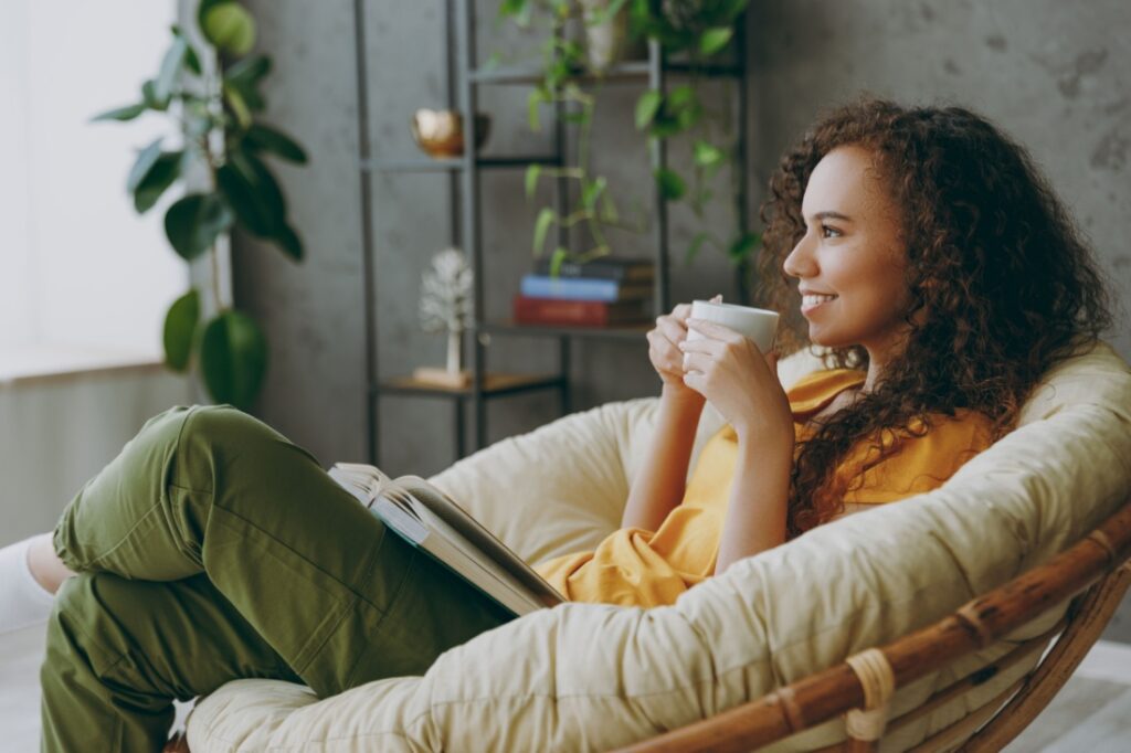 A woman drinks from a mug in a comfortable chair in her home.