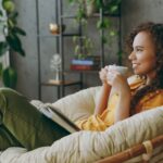 A woman drinks from a mug in a comfortable chair in her home.