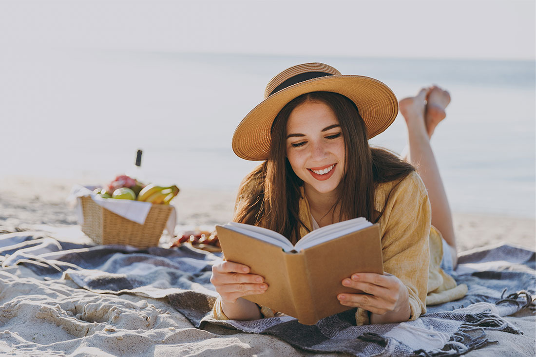 young happy traveler woman in straw hat reading book at beach