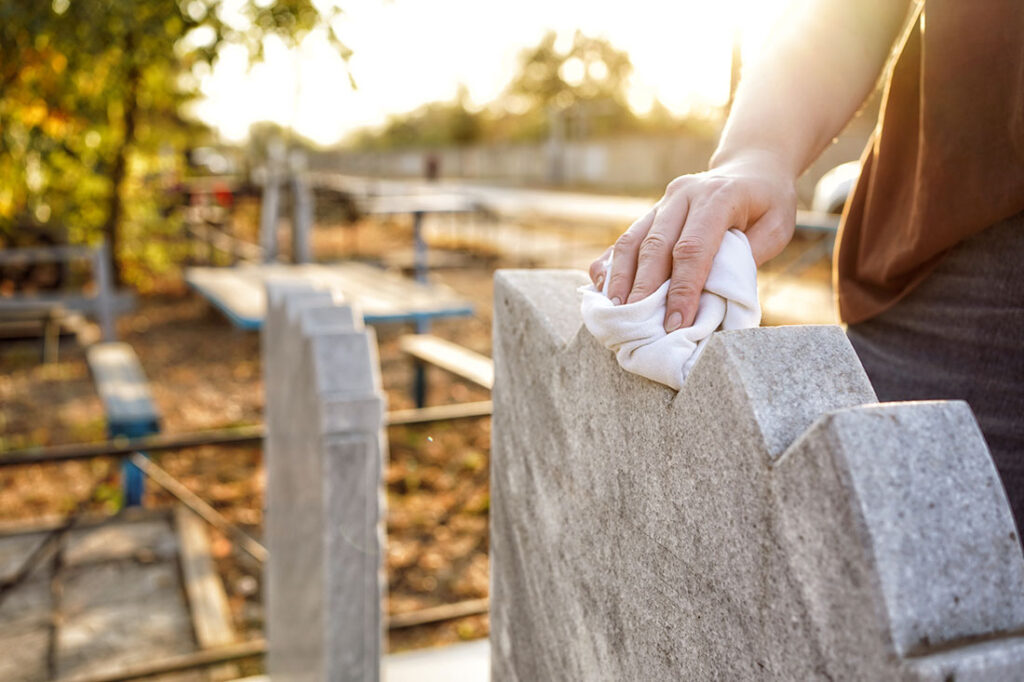 Cleaning the cemetery, a hand washes the grey monument at the grave with a rag.