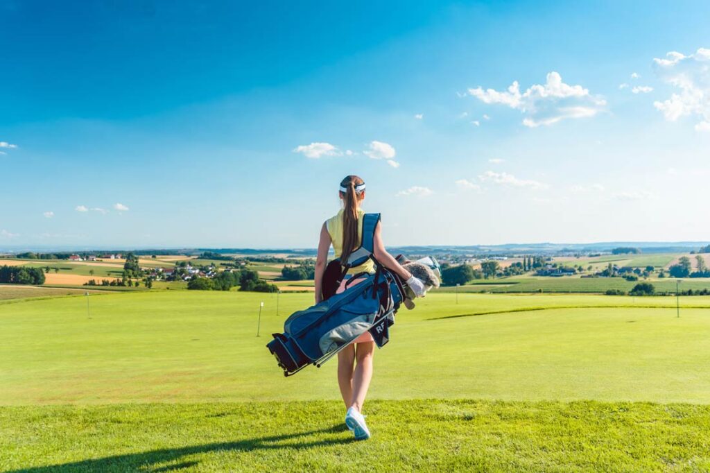 A young female golfer looks out over a sunny golf course