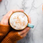 hands holding a pumpkin spice cappuccino in fall colors