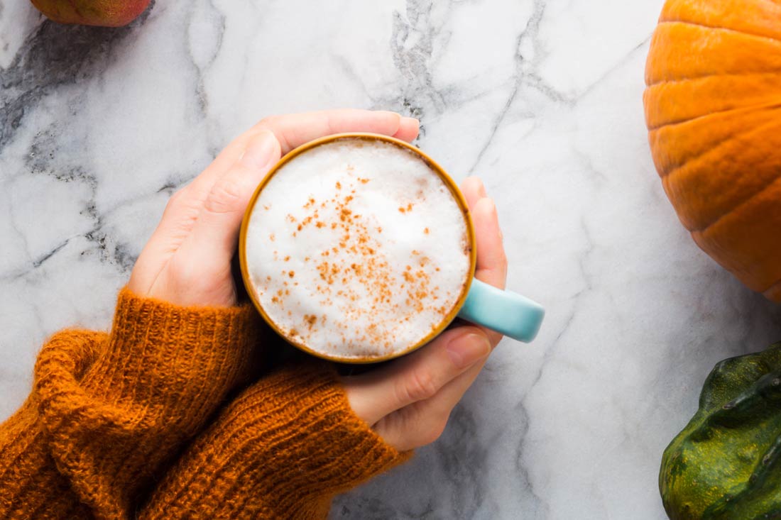 hands holding a pumpkin spice cappuccino in fall colors