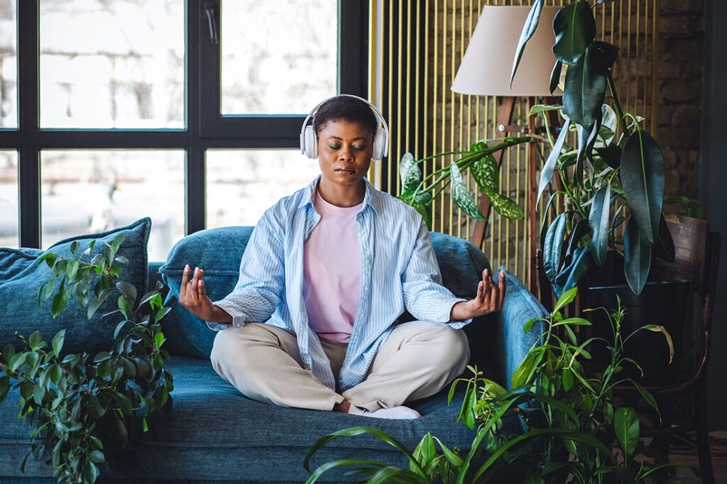 Woman practicing work life balance and meditating, listening to music in headphones at home