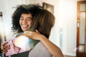 A woman greets another with a hug and gives her a gift.