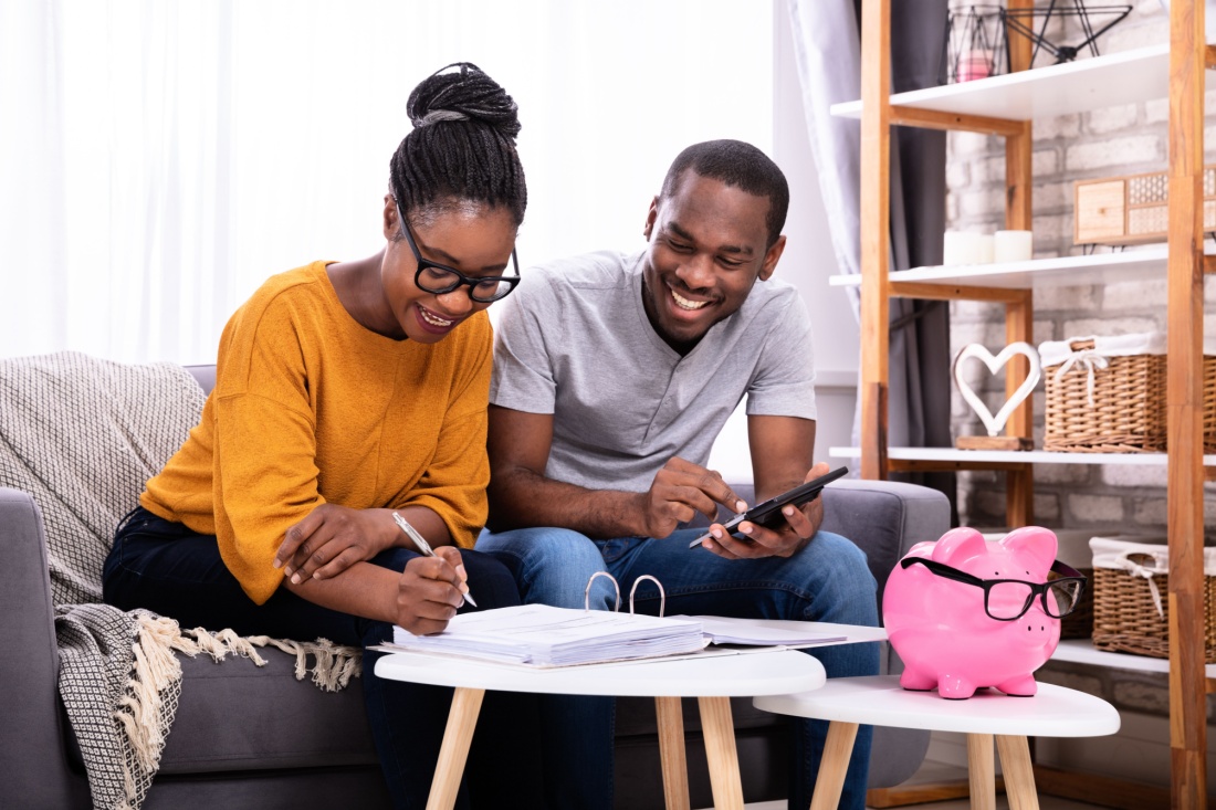 A couple looks over pages in a binder. A piggy bank with glasses sits nearby.