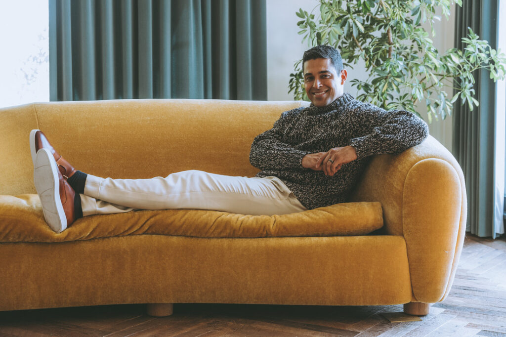 Wilmer Valderrama sitting on a brown couch