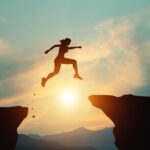 Silhouette of a woman jumping across as gap between two cliffs to reach a finish line flag.