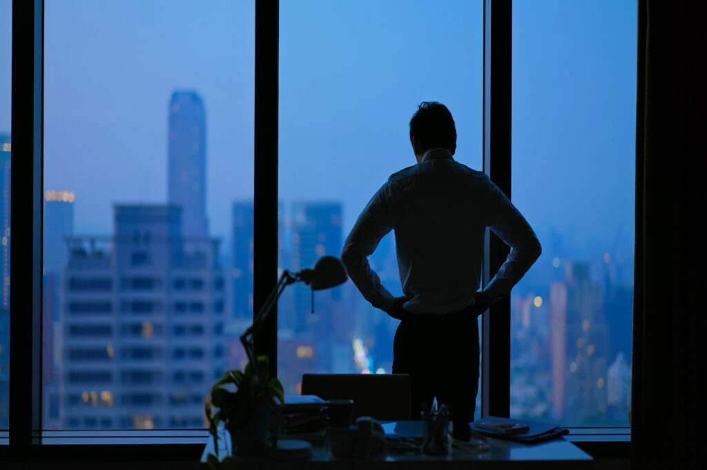 Businessman staring out office window at dark