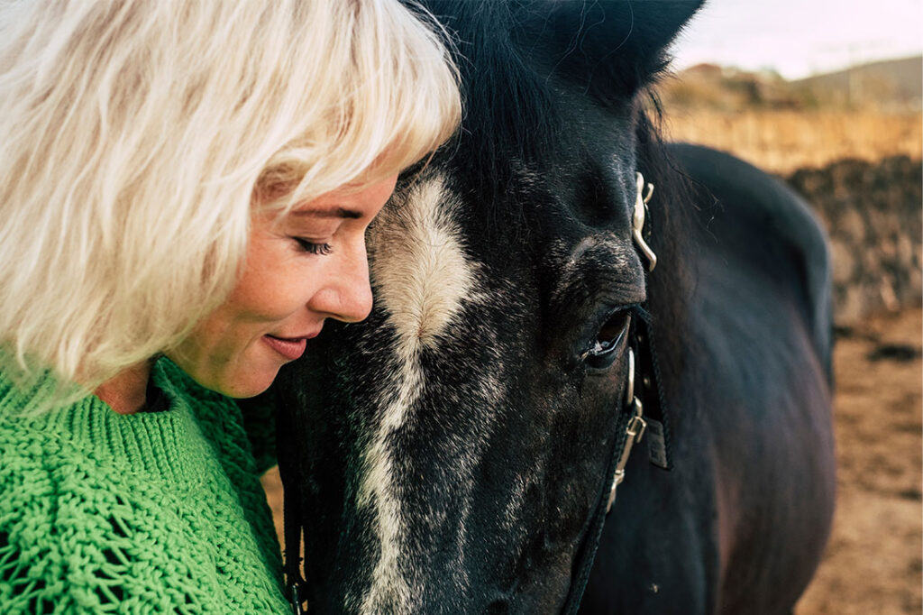 Blonde woman with black horse in outdoor scenic destination hugging