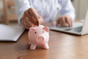 Close up woman putting coin into pink piggy bank, sitting at work desk