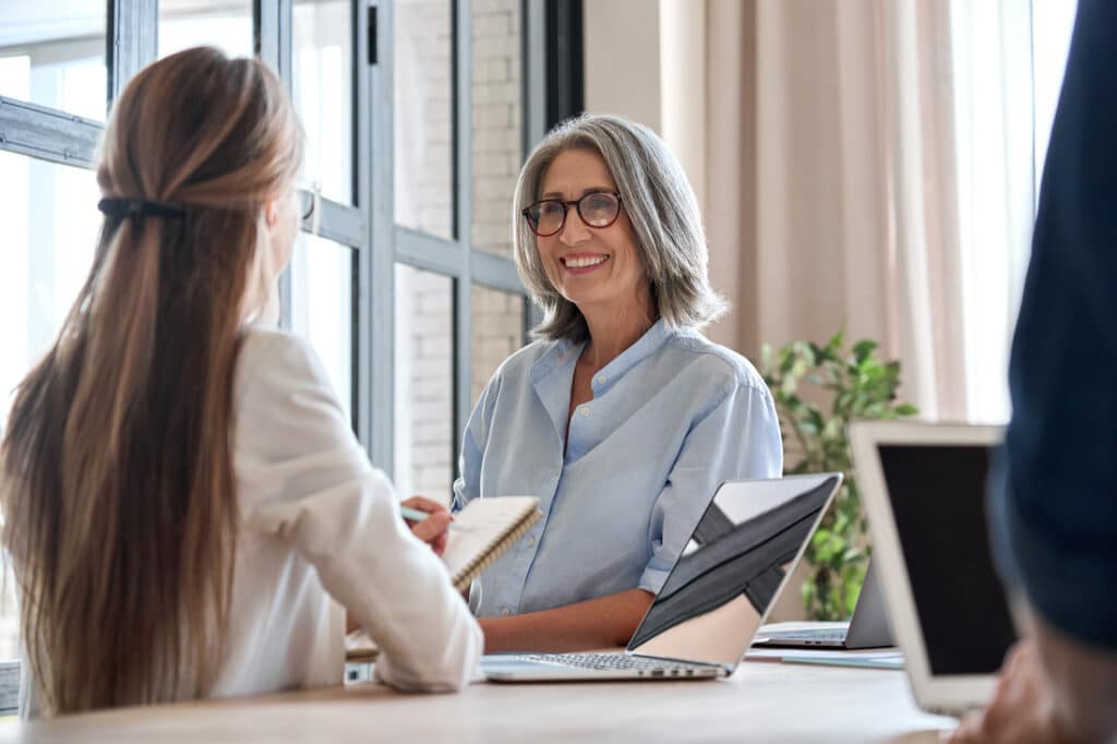 mature woman sitting at a desk speaking with a co-worker