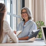 mature woman sitting at a desk speaking with a co-worker