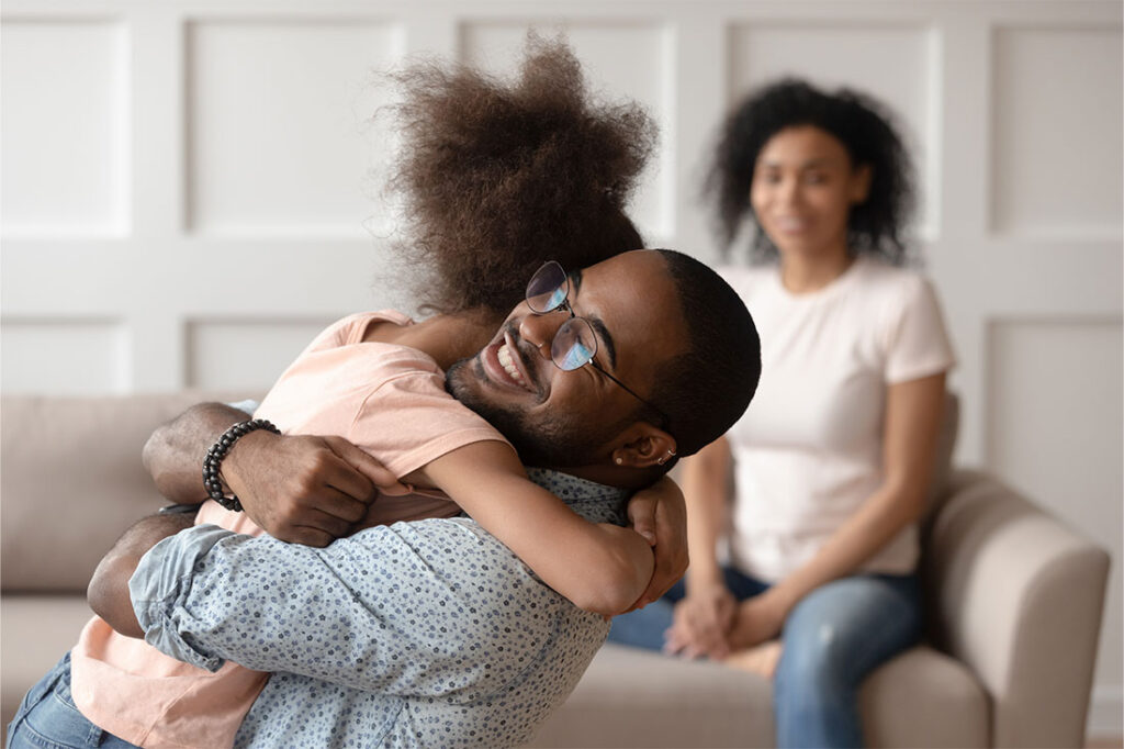 Happy african american dad embracing daughter at home with mother in backdrop smiling