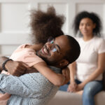 Happy african american dad embracing daughter at home with mother in backdrop smiling