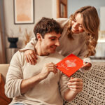 A woman gives a greeting card to her man with the inscription I love you in the living room at home