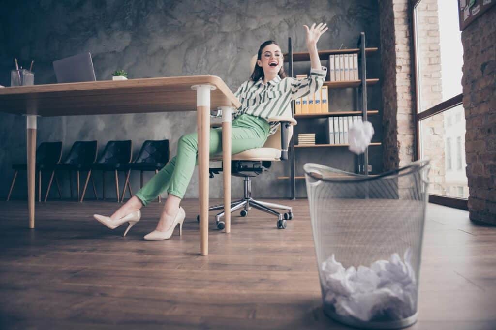 A woman sitting at a desk happily dealing with rejection by throwing away failures