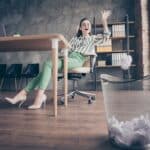 A woman sitting at a desk happily dealing with rejection by throwing away failures