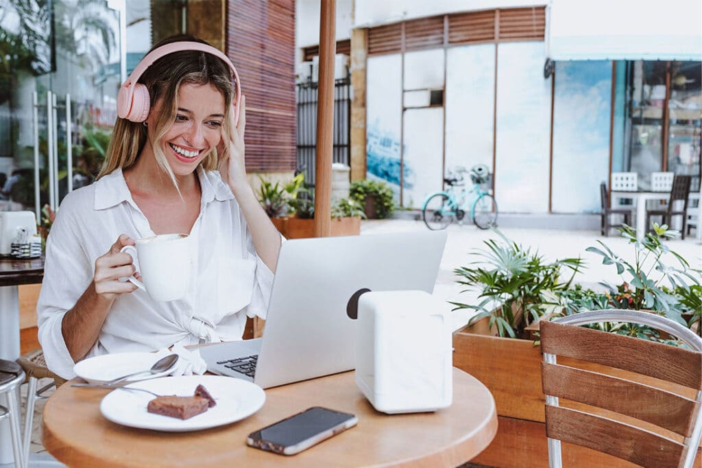 young woman using laptop and drinking coffee at restaurant terrace