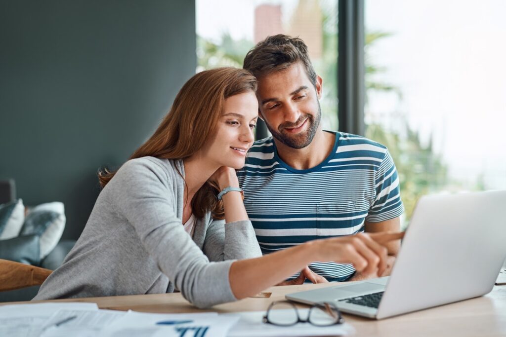 A couple sitting at a table, looking at a laptop