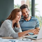 A couple sitting at a table, looking at a laptop